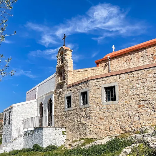 A scenic view of rustic stone church with a bell tower and cross stands under a vivid blue sky in Kastellorizo A scenic view of rustic stone church with a bell tower and cross stands under a vivid blue sky in Kastellorizo