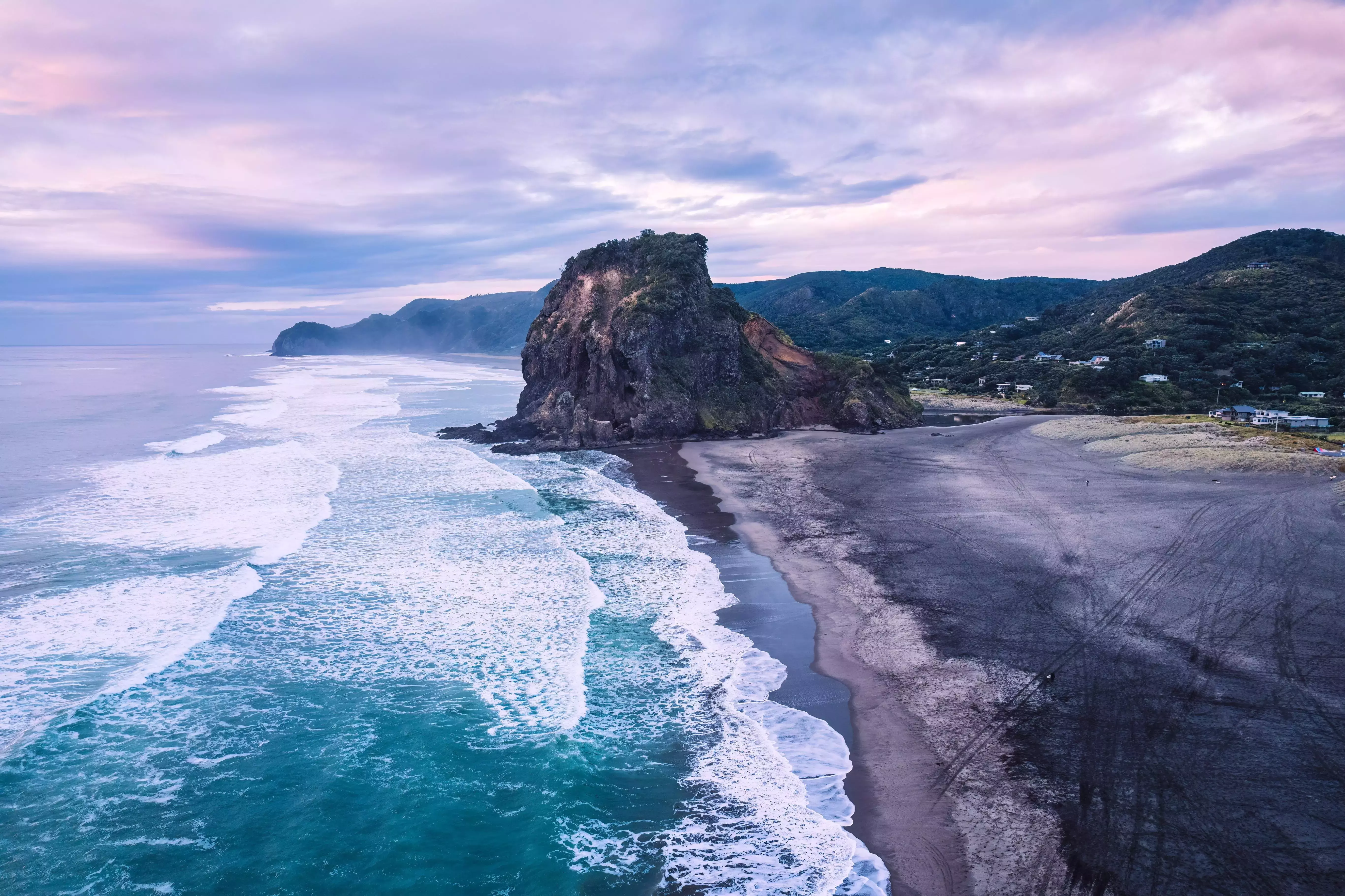 Rugged cliffs and volcanic black sand characterise Piha Beach, New Zealand.