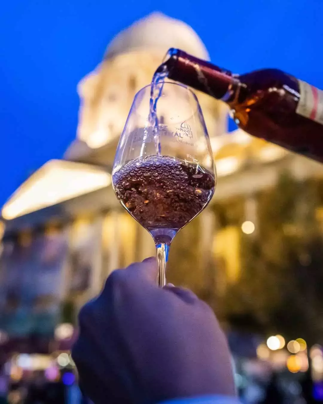 Hungarian wine being poured against a backdrop of food stall tents at Budapest Wine Festival.