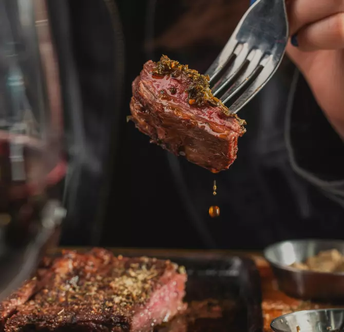 Bite of perfectly cooked steak slathered in chimichurri on a fork in La Cabrera parrilla, Buenos Aires