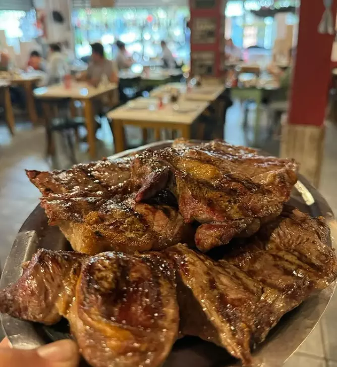 Plate of a steak in front of people sat at restaurant in El Boliche de Nico parrilla, Buenos Aires