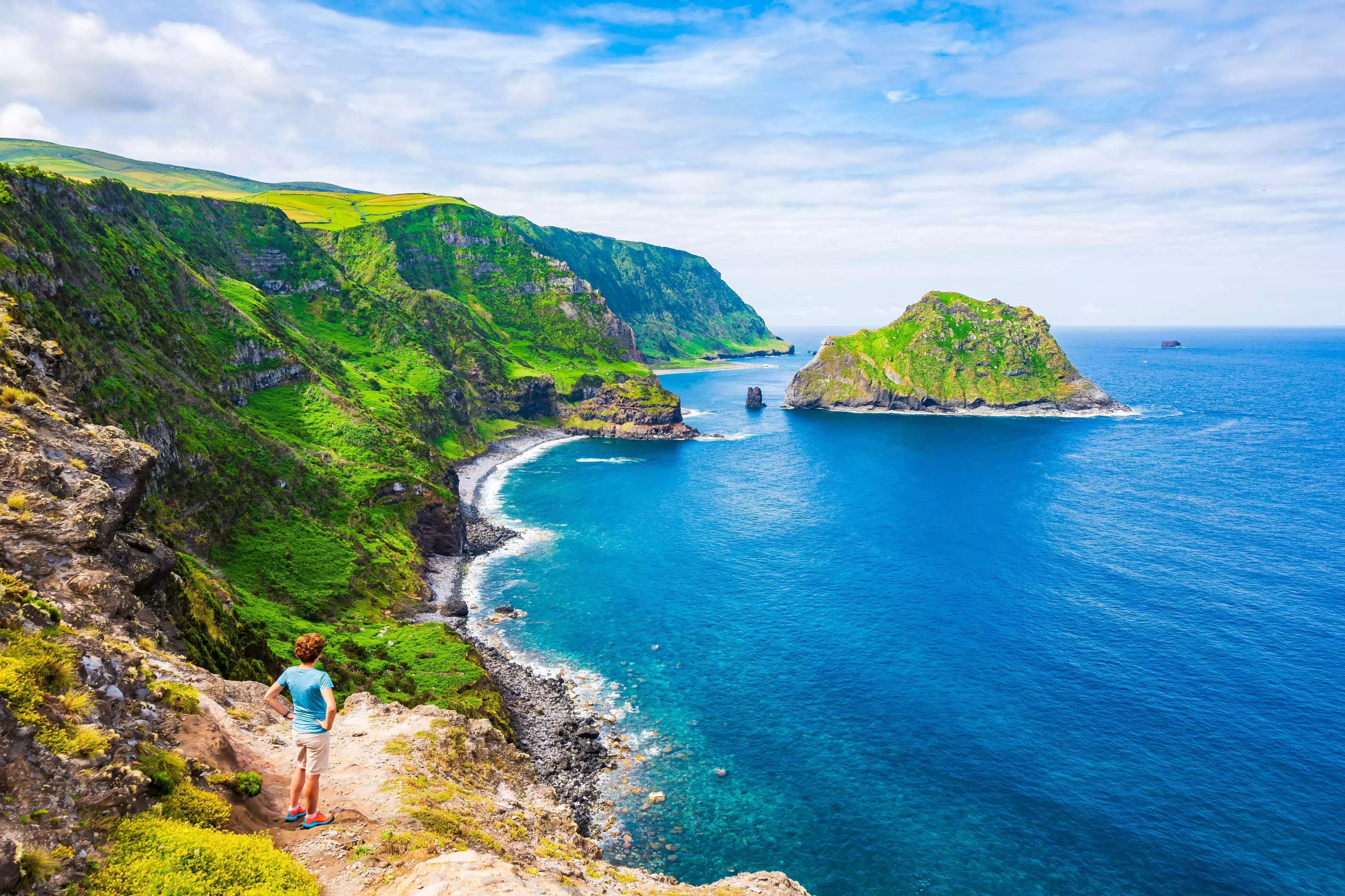 Woman standing on clifftop looking out to sea in Azores, Portugal.