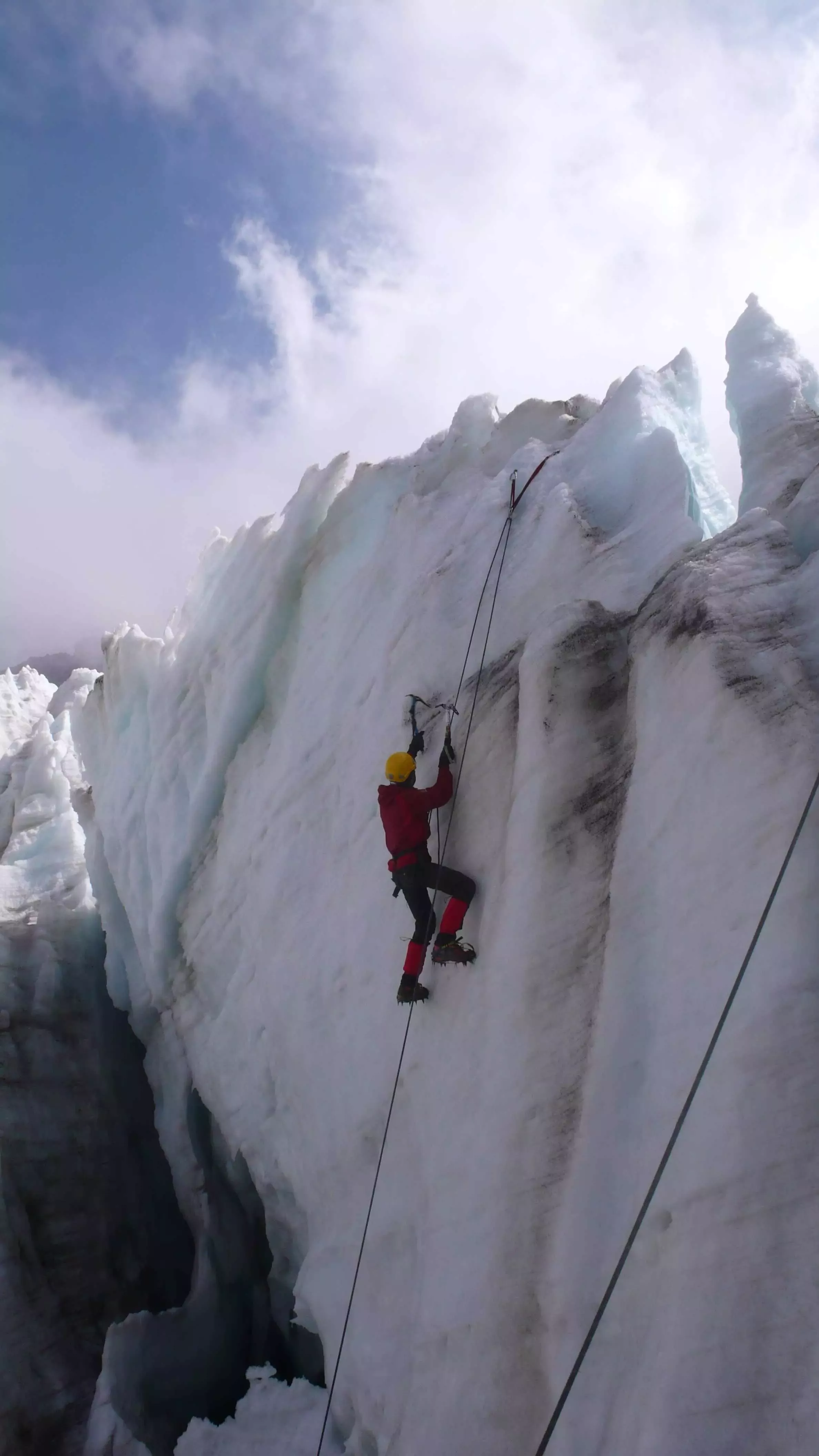 A climber climbing up a large sheet of ice as part of glacier climbing
