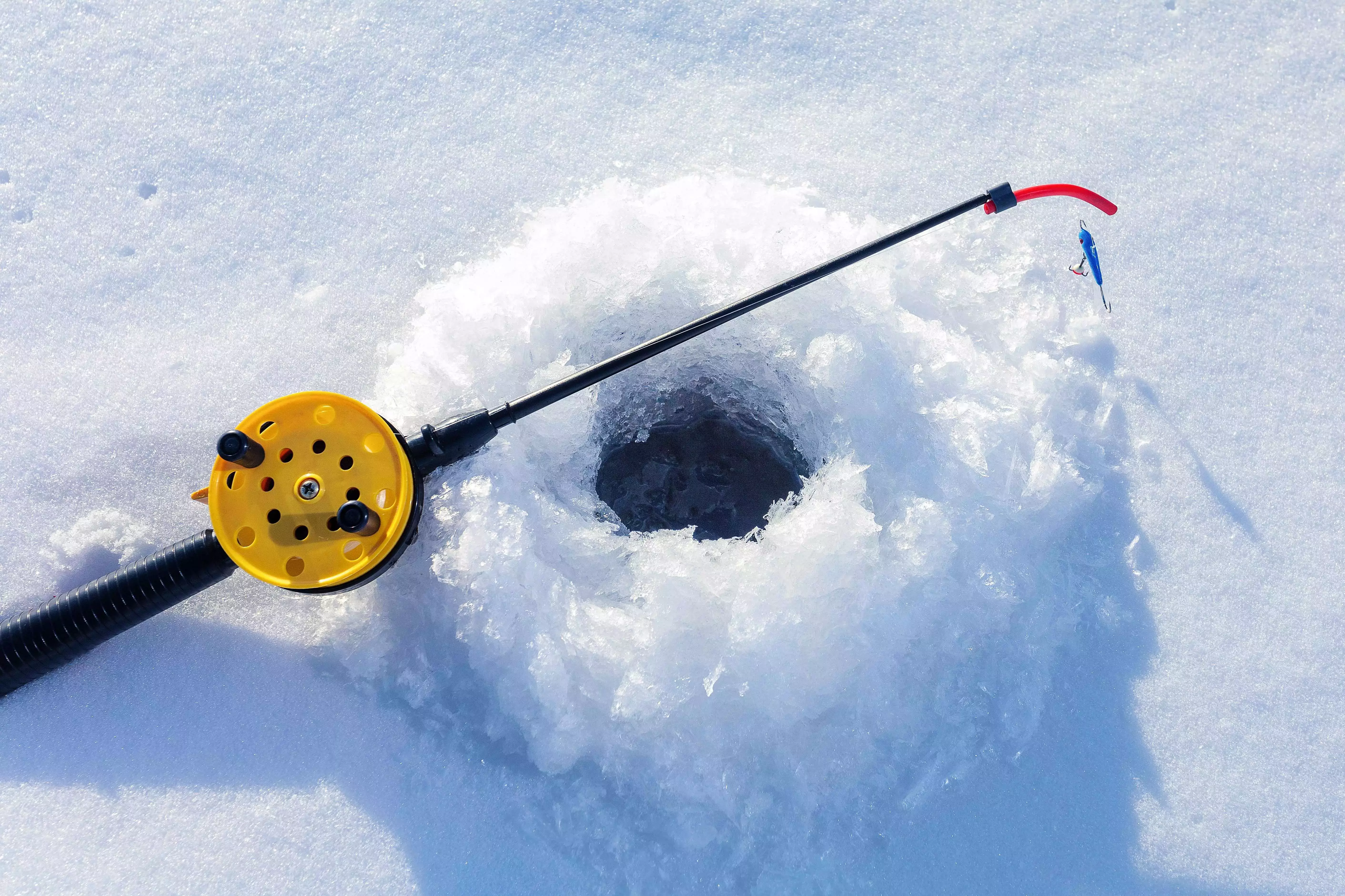 A fishing rod lying on a frozen river with a hole drilled into the ice for ice fishing
