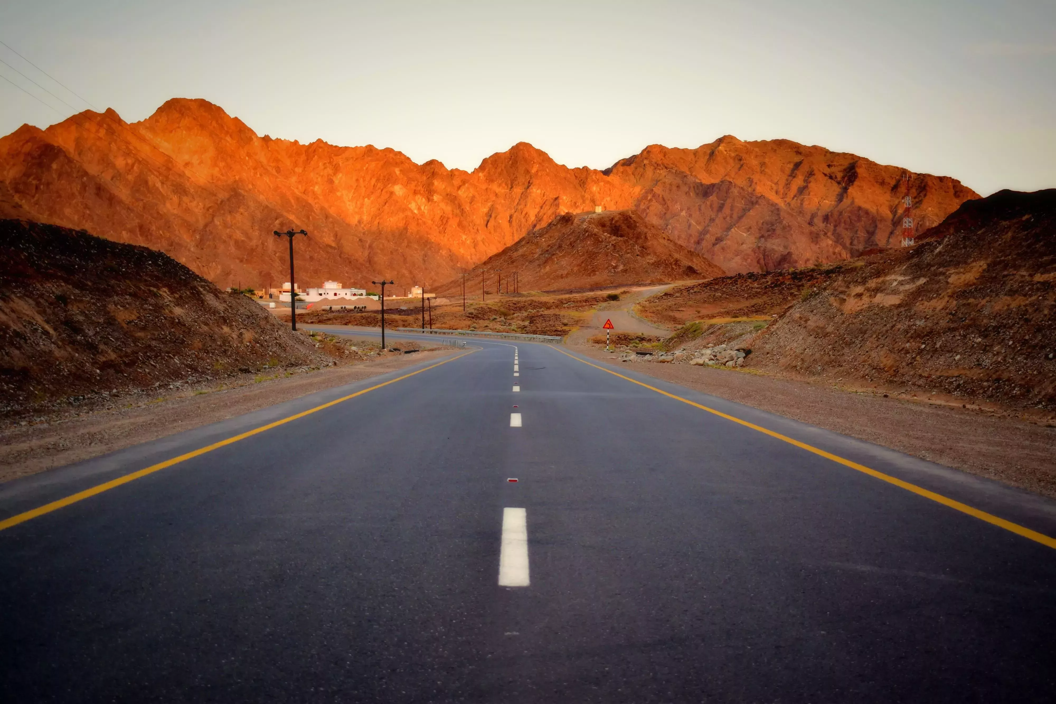 Well-paved road with glowing red mountains ahead in Oman